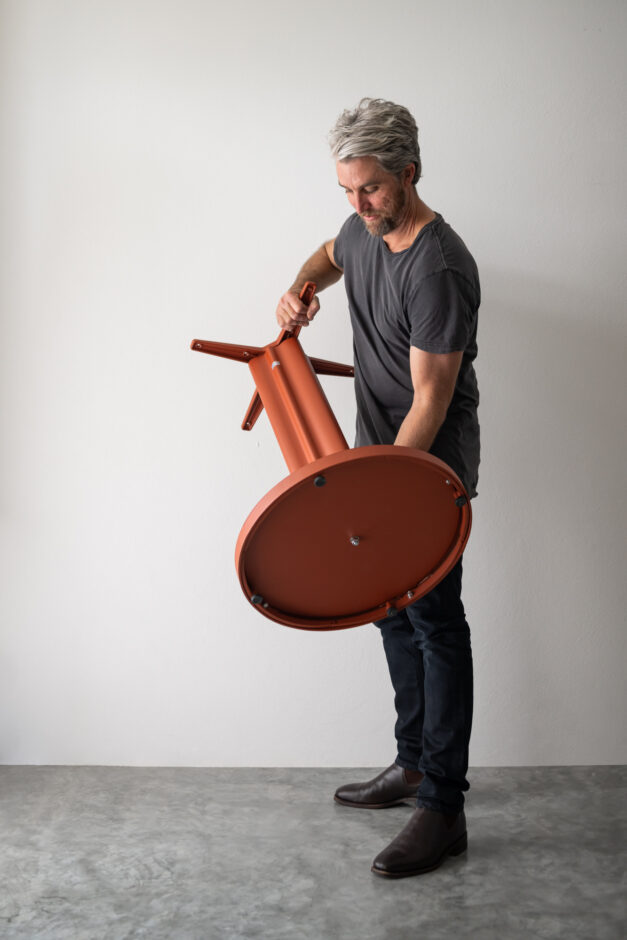 Toby Heyring, NOROCK Co-Inventor and Technical Director, holding the NRxTMH self-stabilising table base in Pindan Red.